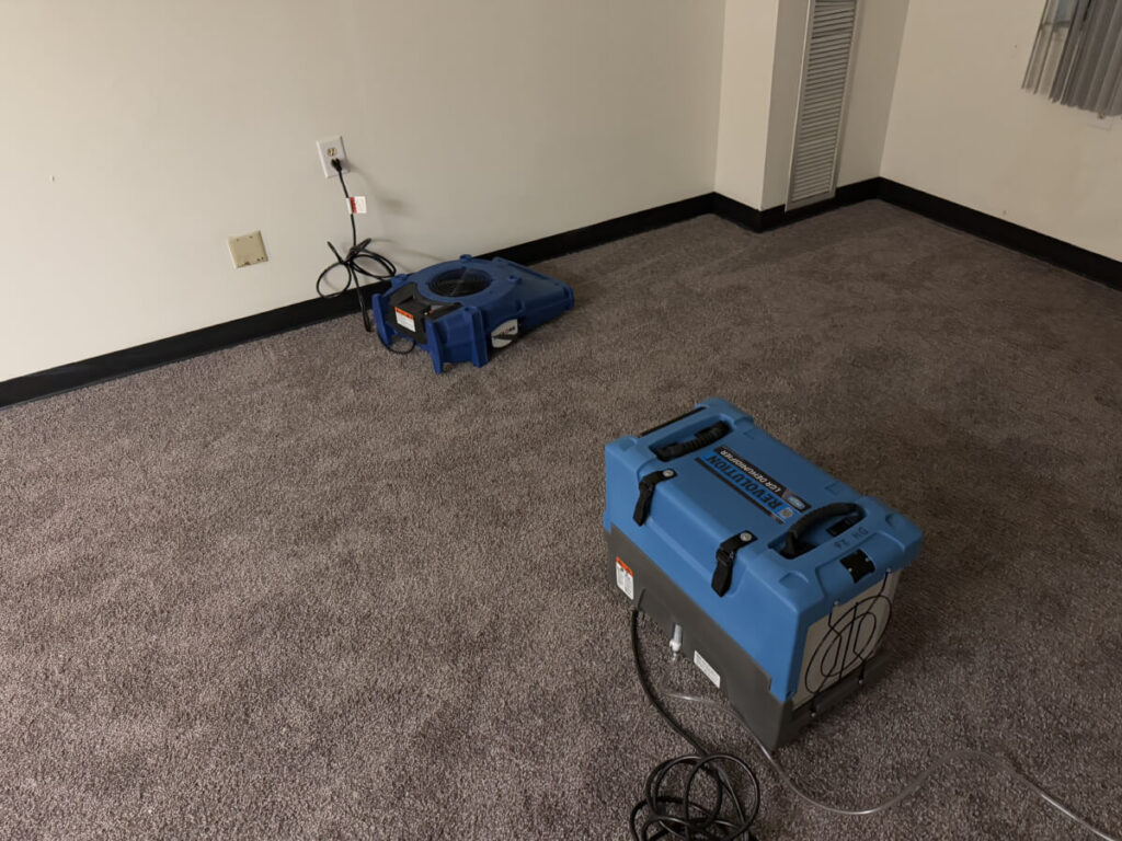 Two pieces of water damage mitigation equipment in room with wet carpet