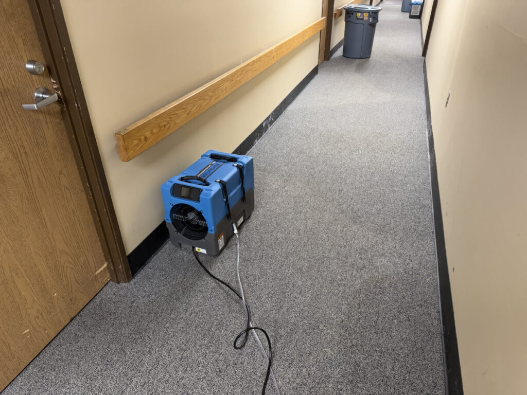 Using water damage mitigation machinery to dry wet carpet in office hallway